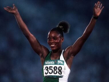 Chioma Ajunwa-Opara stands as a pioneering figure in Nigerian sports history. Born on 25 December 1970 in Umuihiokwu, Ahiazu-Mbaise, Imo State, Nigeria, she rose from humble beginnings to become the first Nigerian to win an Olympic gold medal and the first black African woman to claim gold in a field event. Her victory in the long jump at the 1996 Atlanta Olympics marked a defining moment for African athletics and inspired generations. Ajunwa balanced multiple roles throughout her life, including service as a police officer, participation in both football and track and field at the international level, and later contributions as an educator, philanthropist, and mentor. Her journey highlights resilience, hard work, and dedication in overcoming personal and systemic challenges. This biography explores her life in detail, from her early struggles in a large family to her lasting impact on sports development in Nigeria. Early Life of Chioma Ajunwa Chioma Ajunwa was born on 25 December 1970 in Umuihiokwu, a village in Ahiazu-Mbaise Local Government Area of Imo State, Nigeria. She hails from Imo State, which is located in the southeastern part of the country and is known for its rich cultural heritage, vibrant communities, and contributions to Nigerian education and commerce. Ahiazu-Mbaise features rural settings with strong family ties and traditional values that shaped her upbringing. She grew up as the youngest and only girl among nine children, with six brothers and two sisters. Her family faced significant financial hardship. She described her home as very poor. Her father passed away when she was still young, leaving her mother to raise the large family alone through petty trading and other modest means. This loss placed extra responsibilities on the children, and resources were always stretched thin. Despite these difficulties, Ajunwa showed early promise in sports. She played football with her brothers in the village streets and participated actively in school athletics. Life in rural Imo State during that era involved limited opportunities. Access to quality education and facilities was challenging, yet Ajunwa developed a strong work ethic and determination. She attended primary and secondary school in the area, where her natural talent for running and jumping became evident. Teachers and peers noticed her speed and agility in school competitions. These early experiences built the foundation for her future success, even as economic pressures mounted. At around 18 years old, Ajunwa gained admission to university but could not register because her mother could not afford the tuition fees. Faced with this setback, she considered learning a trade as an automobile mechanic to support herself and her family. Her mother disapproved of the male-dominated field, and Ajunwa eventually set that path aside. This period tested her resolve, but it also pushed her toward opportunities in sports and public service that would define her path. Her mother’s resilience as a single parent who supported nine children left a deep impression, teaching Ajunwa the value of perseverance. The cultural context of Imo State, with its emphasis on community support and education, played a role in her development. Family and local networks provided encouragement, even in tough times. These formative years in a close-knit but resource-scarce environment instilled in her a drive to succeed not just for herself but for her family and community. Ajunwa often reflects on how poverty and early loss motivated her to seize every chance that came her way. Education of Chioma Ajunwa Ajunwa’s formal education began in local schools in Imo State. She completed primary and secondary levels despite financial constraints. Her academic performance was solid, particularly in subjects that supported her athletic interests. The inability to proceed immediately to university after secondary school was a major disappointment, but she did not abandon learning. After her athletic career peaked, she returned to education with renewed focus. She enrolled at the University of Lagos, where she earned a bachelor’s degree in health education or human kinetics. This step allowed her to combine her passion for sports with academic knowledge. She later pursued and completed a master’s degree in sports administration and management at the same institution. These qualifications equipped her with skills for coaching, sports management, and youth development work. Her commitment to education extended beyond personal achievement. Ajunwa has spoken about the importance of continuous learning and how it helped her transition from active sports to other professional roles. She balanced police duties, family, and studies, demonstrating strong time management and dedication. This educational journey reinforced her belief that opportunities for growth exist at any stage of life. Chioma Ajunwa Career Football Career of Chioma Ajunwa Ajunwa began her sporting journey with football. As a young girl, she played with her brothers and developed skills as a striker. She represented Nigeria at the international level, becoming part of the women’s national team, known as the Super Falcons. She participated in the inaugural 1991 FIFA Women’s World Cup in China, marking her as one of the pioneers in Nigerian women’s football on the global stage. Her dual involvement in football and athletics was unusual, but she managed both with enthusiasm. Training schedules often overlapped, yet she trained diligently in both disciplines. This versatility showcased her athleticism and adaptability. Although she faced limited playing time in some camps, her contribution helped pave the way for future generations of female footballers in Nigeria. Transition to Athletics of Chioma Ajunwa Ajunwa shifted her primary focus to track and field, excelling in sprints and long jump. She competed in national championships and quickly rose through the ranks. Her early successes included victories at African Championships. In 1989 in Lagos, she won gold in the long jump. She repeated similar feats in subsequent years, building a reputation as a formidable competitor. She also participated in the 100 meters and relay events, contributing to team successes. Her natural speed and jumping ability, honed from childhood activities, gave her an edge. Despite setbacks, she maintained consistency in domestic competitions, winning multiple Nigerian titles in the long jump. Challenges and Comeback of Chioma Ajunwa In 1992, Ajunwa faced a significant challenge when she tested positive in a drug test, leading to a four-year ban. She maintained her innocence throughout but served the suspension. This period was difficult, as it halted her momentum at a promising time. She used the time for reflection and preparation, returning stronger after the ban lifted. Her comeback demonstrated remarkable mental strength. She qualified for the 1996 Olympics and delivered a historic performance. This phase of her career highlighted her ability to overcome adversity and refocus on goals. Olympic Success and Peak Performance of Chioma Ajunwa At the 1996 Summer Olympics in Atlanta, Ajunwa achieved her greatest feat. She won the gold medal in the women’s long jump with a distance of 7.12 meters on her first attempt in the final. This jump secured Nigeria’s first Olympic gold medal and made her the first black African woman to win gold in a field event. The moment elevated her status as a national hero and African sports icon. She also competed in the 100 meters and 4×100 meters relay at the same Games, reaching the semifinals and contributing to the team. Her long jump record stood as an African record for 25 years until it was surpassed in 2021. The victory brought immense pride to Nigeria and highlighted the potential of African athletes on the world stage. Police Service Career of Chioma Ajunwa Ajunwa joined the Nigeria Police Force around 1988, serving for over 35 years while pursuing sports. She rose through the ranks, eventually becoming a Deputy Commissioner of Police (DCP, retired). Her service included roles such as Divisional Police Officer at Meiran Police Station in Lagos. She balanced demanding police duties with athletic training, often training early in the morning before shifts. She received promotions in recognition of her contributions, including to DCP in 2023 before retiring. Her police career exemplified discipline and public service. Colleagues and superiors valued her commitment, and she served as a role model for integrating sports excellence with professional responsibilities. Post-Athletics Contributions of Chioma Ajunwa After retiring from competitive sports in 2002, Ajunwa focused on education, mentoring, and community work. She earned advanced degrees and engaged in sports administration. In December 2017, she launched the Chioma Ajunwa-Opara Foundation to discover and nurture young Nigerian sports talents. The foundation has organized championships and collaborated with state governments to support under-16 athletes. She has advocated against doping in sports and promoted fair play. Through mentorship programs and public speaking, she shares lessons from her journey to inspire young people. Her work emphasizes education, hard work, and integrity. Achievements of Chioma Ajunwa Ajunwa accumulated numerous accomplishments across football and athletics. Key highlights include her Olympic gold, multiple African Championship titles in long jump and relays, and national records. She won medals at Commonwealth Games and All-Africa Games. Her participation in both the Women’s World Cup and Olympics as a dual-sport athlete remains unique. She set personal bests such as 7.12 meters in long jump, strong times in sprints, and contributed to team relays. These feats brought international recognition and elevated Nigerian sports. Awards of Chioma Ajunwa Ajunwa received several honors for her contributions. She was awarded the Member of the Order of the Niger (MON). She earned recognitions from Nigerian presidents for sports and national service. Her Olympic achievement led to national celebrations and honors. Additional awards came from sports bodies and community organizations for her foundation work and anti-doping efforts. These accolades reflect her impact as an athlete, officer, and philanthropist. Personal Life of Chioma Ajunwa Ajunwa is married to Howell Chidera (also referred to as Howell Opara in some contexts). She is a mother of three children, including triplets born after years of waiting. Family life brought her joy after the demands of her career. She has spoken about the support from her husband, a fellow police officer, and the challenges of balancing motherhood with professional roles. She remains connected to her roots in Imo State while living primarily in Lagos due to her work. Her personal experiences with loss, poverty, and delayed family milestones have deepened her empathy and commitment to helping others. Legacy and Impact of Chioma Ajunwa Ajunwa’s legacy extends beyond medals. She symbolizes hope and possibility for young Nigerians facing similar obstacles. Her foundation continues to identify talents and provide opportunities. She promotes sports as a tool for development, discipline, and national unity. Her story encourages education and resilience, influencing policies and youth programs in Nigeria. As a retired DCP, educator, and mentor, she advocates for ethical sports and community empowerment. Her influence reaches athletics, law enforcement, and social initiatives. Conclusion Chioma Ajunwa-Opara’s life illustrates the power of determination and adaptability. From a poor village home in Imo State to Olympic glory and continued service, she has left an indelible mark. Her achievements continue to inspire, and her ongoing work through the foundation ensures her impact endures for future generations. FAQs What is Chioma Ajunwa known for? Chioma Ajunwa is known for winning Nigeria’s first individual Olympic gold medal in the long jump at the 1996 Atlanta Games. When and where was Chioma Ajunwa born? She was born on 25 December 1970 in Umuihiokwu, Ahiazu-Mbaise, Imo State, Nigeria. Did Chioma Ajunwa play football? Yes, she represented Nigeria in football at the 1991 FIFA Women’s World Cup before focusing more on athletics. What is the Chioma Ajunwa Foundation? It is a foundation she launched in 2017 to discover and support young Nigerian sports talents through training and competitions. How long did Chioma Ajunwa serve in the Nigeria Police Force? She served for over 35 years, retiring as a Deputy Commissioner of Police. What degrees does Chioma Ajunwa hold? She holds a bachelor’s degree in health education or human kinetics and a master’s in sports administration and management from the University of Lagos.